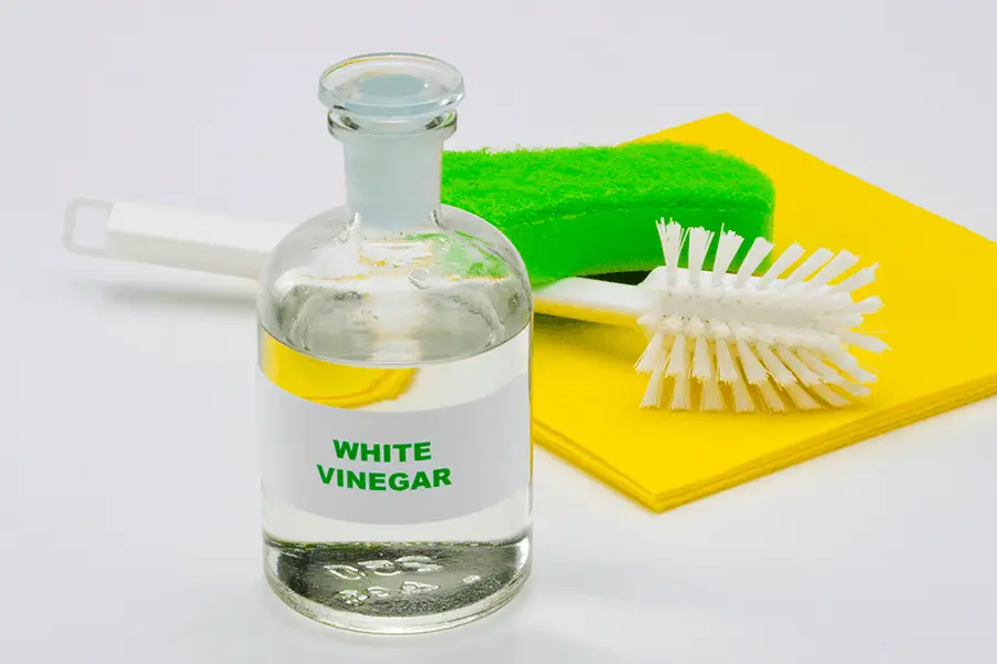 White vinegar in a glass bottle with cleaning supplies in the background
