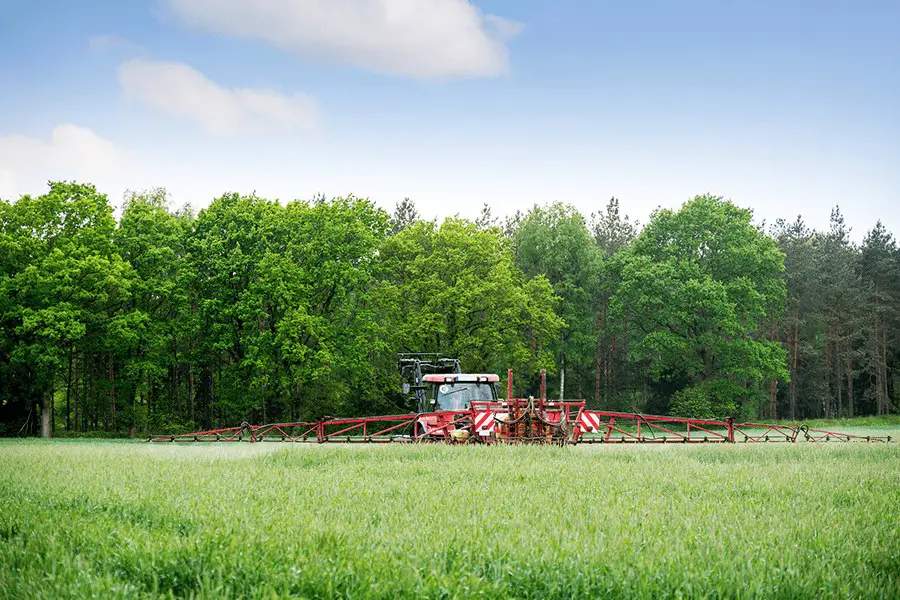 Old red tractor spraying herbicide on a field near the forest