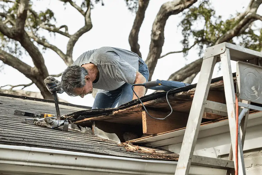 Man using crowbar to remove rotten wood from leaky roof